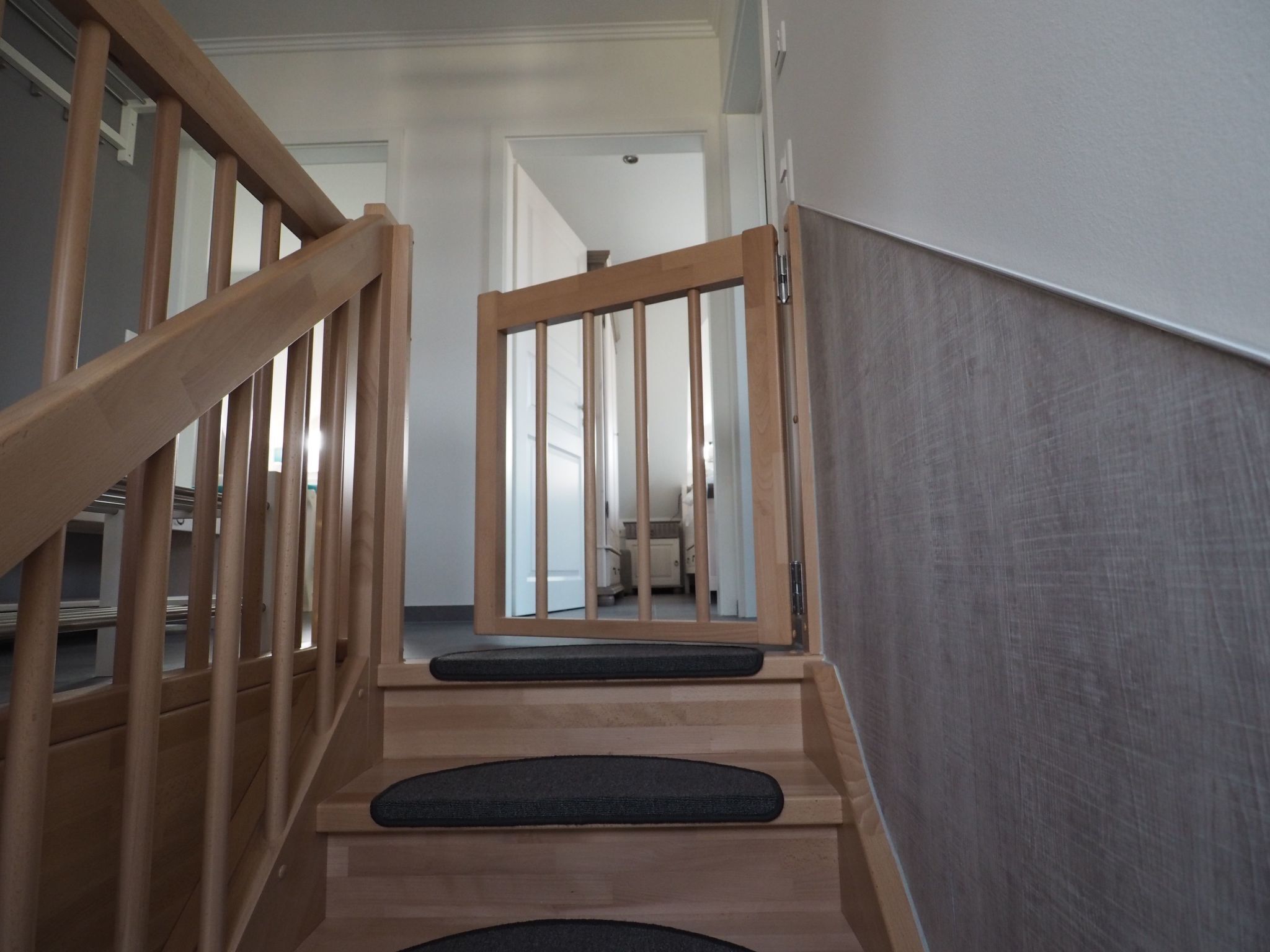 Een houten trap met een leuning en een donkere mat onderaan.