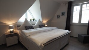 A bedroom with a large bed, two bedside tables, a window, and a small stool. - Traumbrise by Interhome (Rerik)