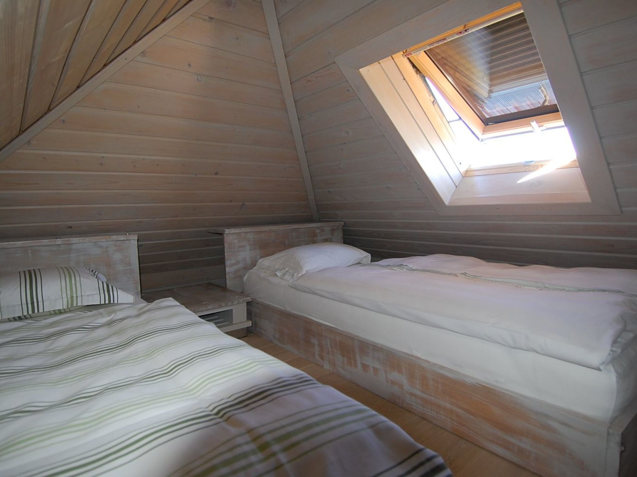 Un pequeño y acogedor dormitorio en el ático con dos camas, un tragaluz y paredes de madera.