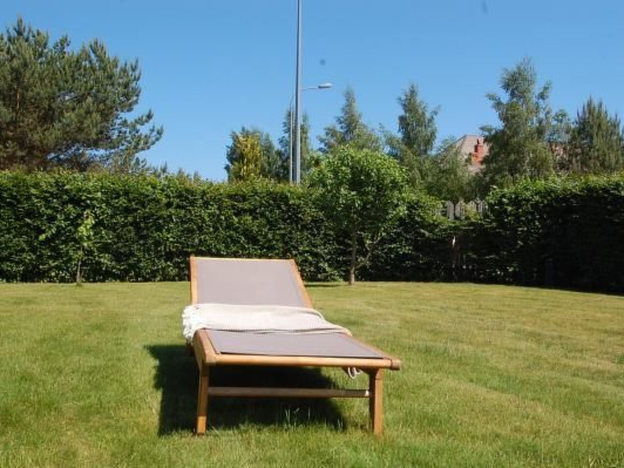 A single lounge chair in a grassy area with a hedge and trees in the background.