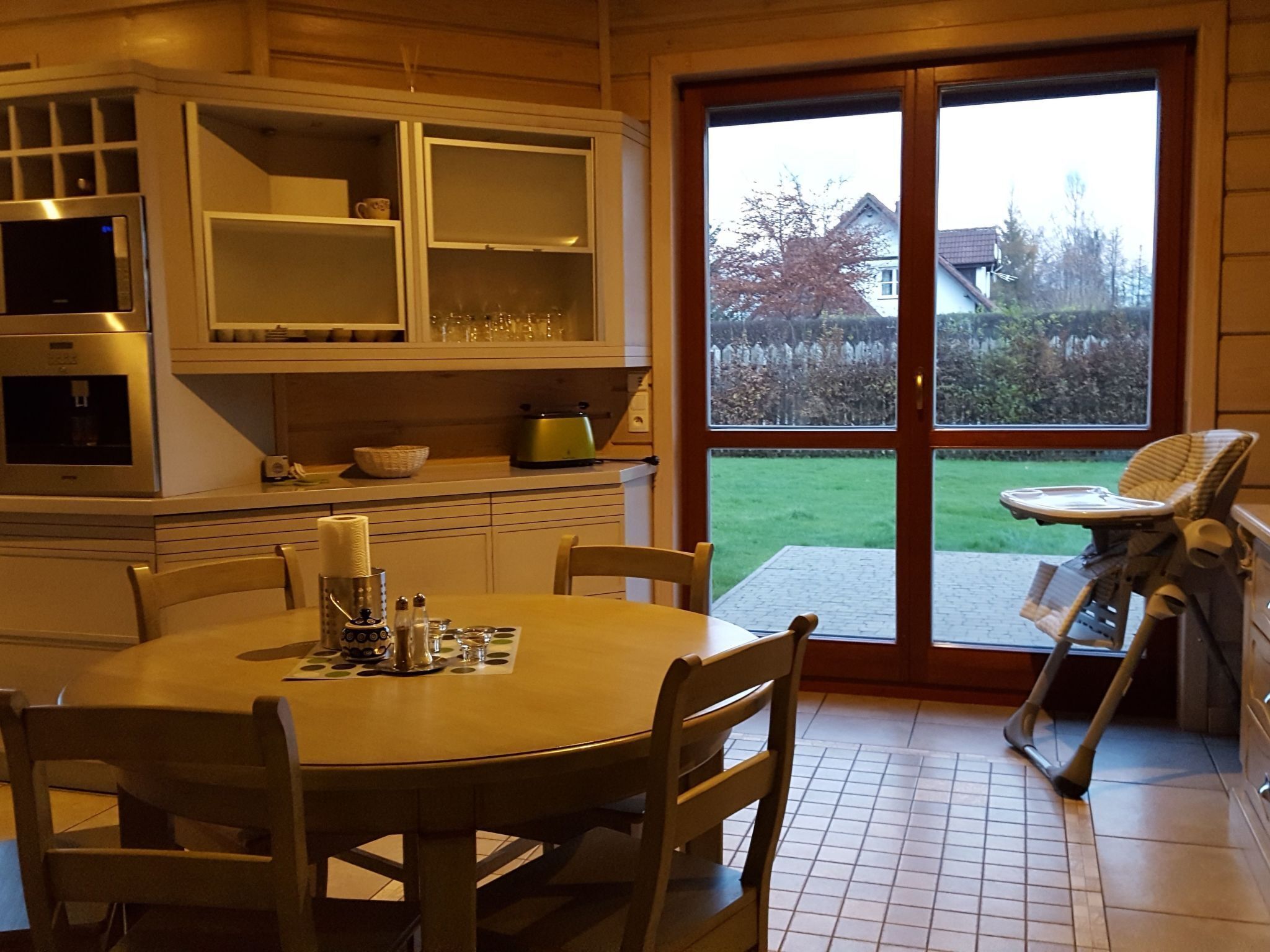A kitchen with a dining table, chairs, and a view of the backyard through a glass door.