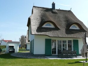 A thatched-roof house with a white exterior and green shutters, a small patio with outdoor seating, and a gravel driveway. - Traumfänger by Interhome (Rerik)