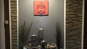 A stone Buddha statue in a garden setting with a stone wall backdrop and a framed Buddha image above. - an der Kaschubischen Seenplatte by Interhome (Sierakowice)