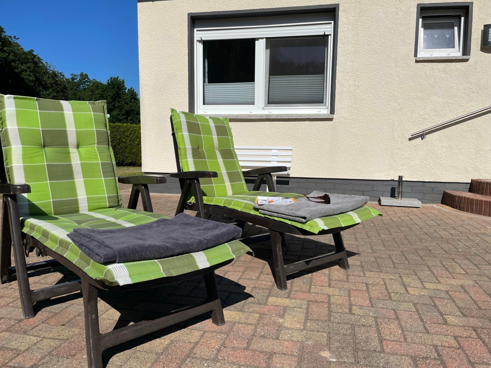 Two lounge chairs with green and white checkered cushions, a small table, and a grey towel on the ground.