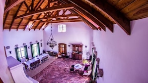 Een ruime kamer met een hoog houten plafond, een eethoek met een lange tafel en een gezellige zithoek met een kamerkleed.