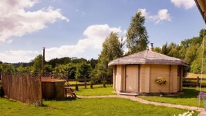 Eine Holzhütte mit einem Strohdach, umgeben von einem Holzzaun und einem Blumengarten.