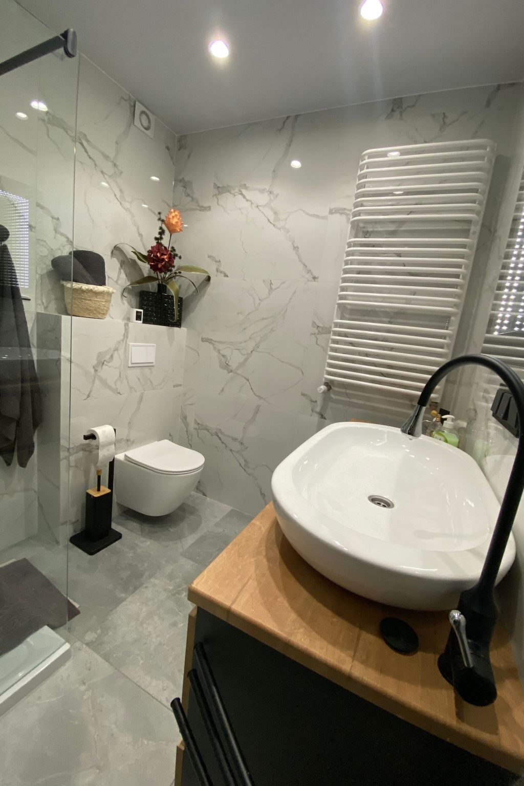 A modern bathroom with a marble backsplash, a white toilet, a wooden vanity with a sink, and a glass shower enclosure.