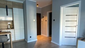 Una sala de estar moderna con una mesa de centro redonda, un área de cocina con una mesa de comedor y sillas, y un pasillo que conduce a un dormitorio.