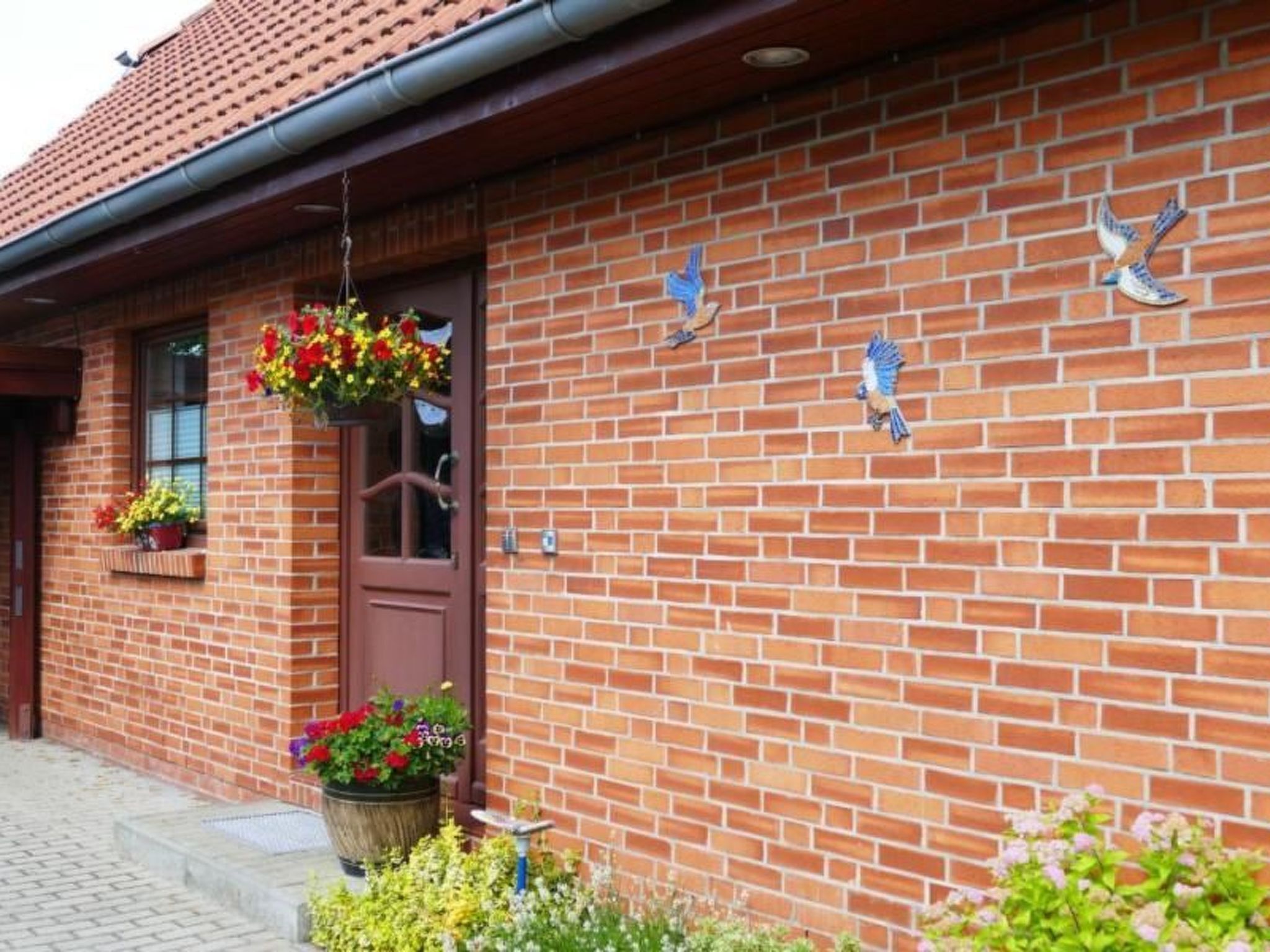 A brick building with a brown door, hanging flower baskets, and bird decorations on the wall.