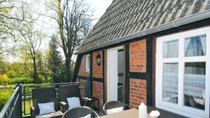 Een terras met rieten meubels en een tafel, een bakstenen muur en een raam met kantgordijnen.