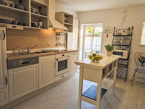 Une cuisine moderne avec des meubles blancs, une cuisinière en acier inoxydable et un saladier de fruits posé sur l’îlot central.