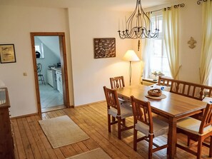 Un comedor con una mesa y sillas de madera, una araña, una lámpara y una cocina al fondo.