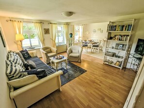 Ein Wohnzimmer mit Sofa, Sesseln, Couchtisch, Bücherregal und Fernseher.