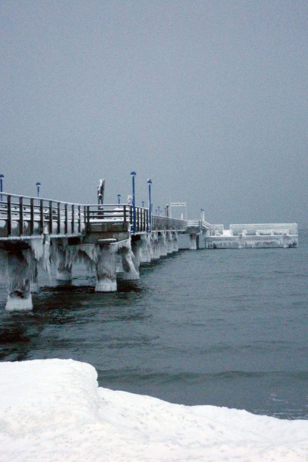 A pier extending into a body of water with a snow-covered foreground.