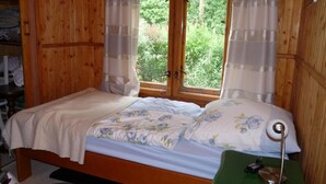 Une pièce de cabane en bois comprenant un lit, une fenêtre avec des rideaux, un bureau avec une lampe et un aspirateur.