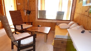 Une pièce chaleureuse avec un plancher en bois, un canapé, un fauteuil, une petite table et un téléviseur fixé au mur.