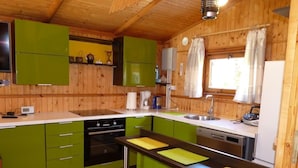 Une cuisine de taille réduite avec des meubles de couleur verte, une cuisinière, un four, un évier et une fenêtre avec des rideaux.