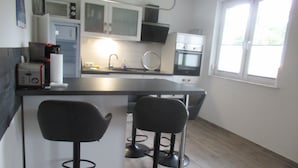 Une cuisine compacte dotée d’un îlot central, de deux tabourets de bar, d’un four à micro-ondes, d’un grille-pain et d’une fenêtre avec des stores.