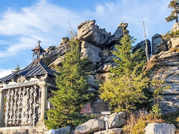 A chapel with a cross on top, surrounded by rocks and trees.