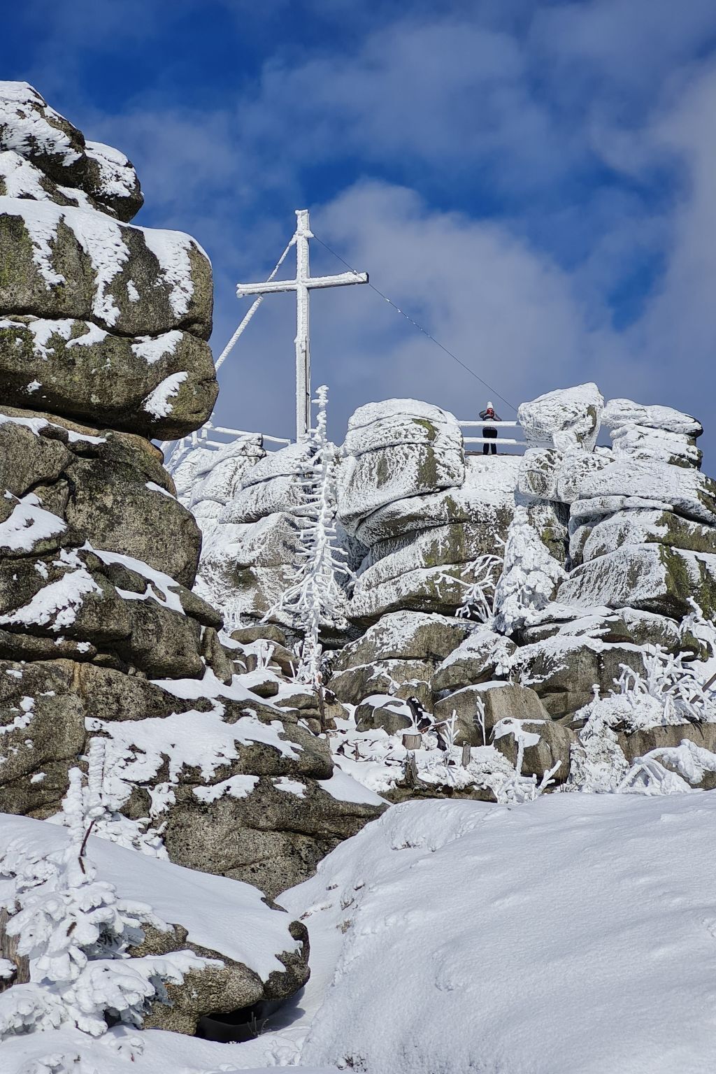 Schneebedeckte Landschaft mit großen Felsen und einem Kruzifix im Hintergrund.