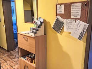 Een hotel receptie met een houten balie, een spiegel en diverse informatieposters aan de muur.