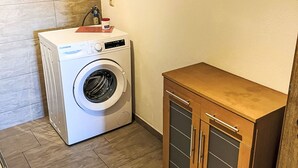Une petite buanderie équipée d’un lave-linge à chargement frontal, d’un petit meuble de rangement et d’un plancher en bois.