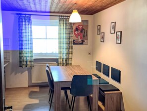Een eetgedeelte met een houten tafel, stoelen, een radiator en een raam met gordijnen.