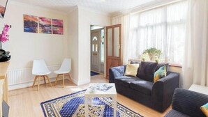 A living room with a sofa, two chairs, a coffee table, and a patterned rug. There are three paintings on the wall and a ceiling light fixture. - Schönes Haus in Orpington by Interhome (St. Mary Cray)