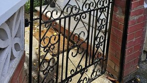 A white door with a decorative glass panel, a black wrought iron gate, and a brick wall. - Schönes Haus in Orpington by Interhome (St. Mary Cray)