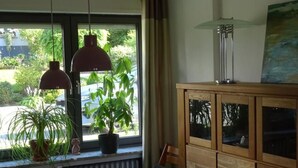 Ein Essbereich mit Tisch, Stühlen, Topfpflanzen, einer Schranke mit Glastüren und Pendelleuchten.