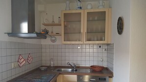 Cocina compacta con lavavajillas, fregadero y estufa. Hay armarios sobre el fregadero y una repisa con objetos decorativos.