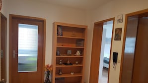 Un pasillo con una estantería de madera, un florero con flores y una puerta que da a otra habitación.