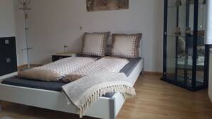Un dormitorio con cama, mesitas de noche, lámpara, un cuadro y un aparador con puertas de cristal.