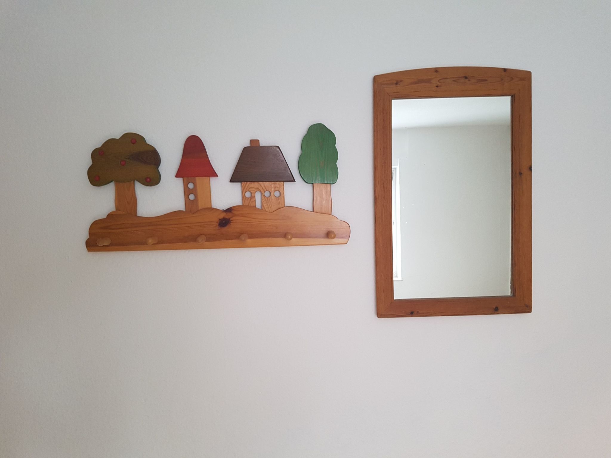 Ein Holzregal mit drei baumförmigen Dekorationen und einem Spiegel an einer schlichten Wand.