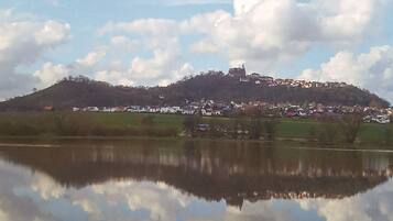 Un pueblo en la cima de una colina con una estructura similar a un castillo, rodeado de casas y una masa de agua que refleja el cielo y las nubes.