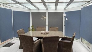 Un patio cubierto con techo de vidrio, una mesa redonda y sillas de mimbre.