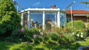 Un invernadero con techo de cristal, rodeado de un jardín con diversas flores y plantas.