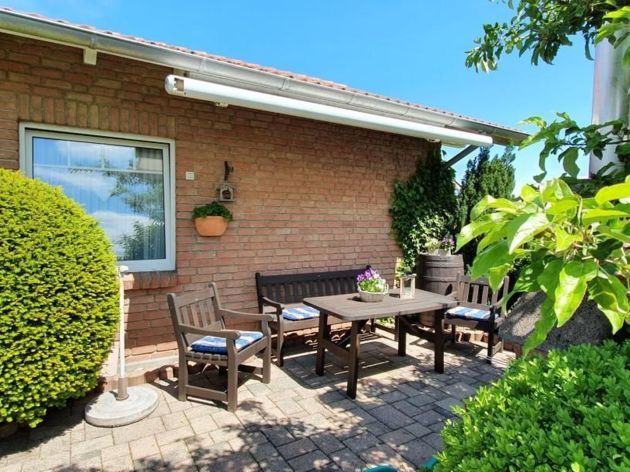 Eine Terrasse mit Backsteinmauer, einem Fenster und einem Tisch mit Stühlen.