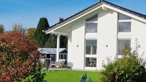 Una moderna casa a due piani con facciata bianca, ampie finestre e una veranda coperta con mobili da esterno.