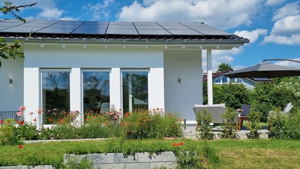 Una casa moderna con pannelli solari, ampie finestre e un giardino con fiori rossi.