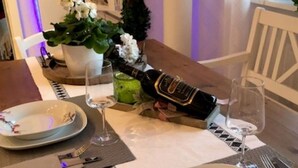 Ein Esstisch ist gedeckt mit Tellern, Besteck, einer Champagnerflasche und Gläsern.
