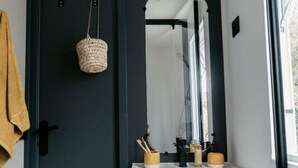 Casa de banho com porta escura, lavatório branco, espelho e porta-toalhas.