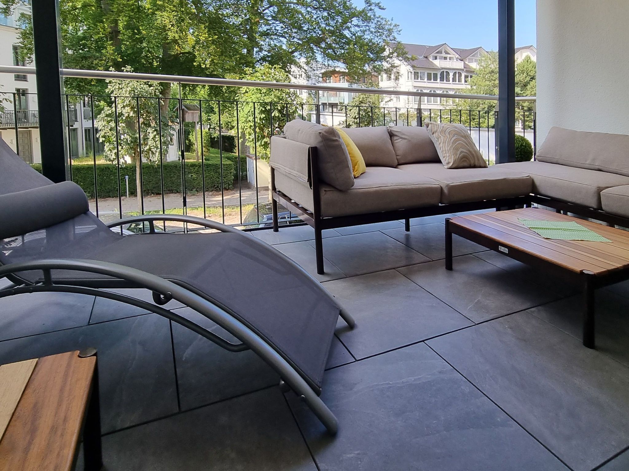 A balcony with a sofa and a table, a chair, and a view of a residential area.