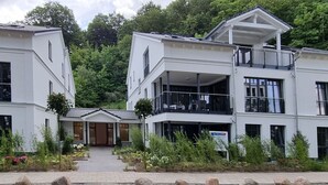 A modern building with a central entrance, multiple balconies, and a garden area with rocks and plants. - Strandblick by Interhome (Binz)