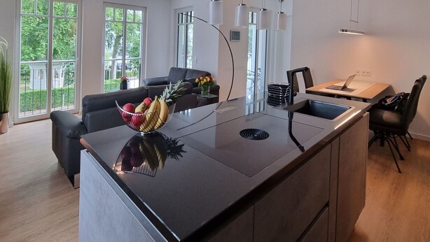 A modern kitchen with a central island, a dining area with a sofa, and large windows providing natural light. - Strandblick by Interhome (Binz)