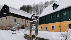 A snow-covered building with a stone entrance, a green and yellow facade, and a barn in the background. - Wohnung in Bad Gottleuba by Interhome (Bad Gottleuba)