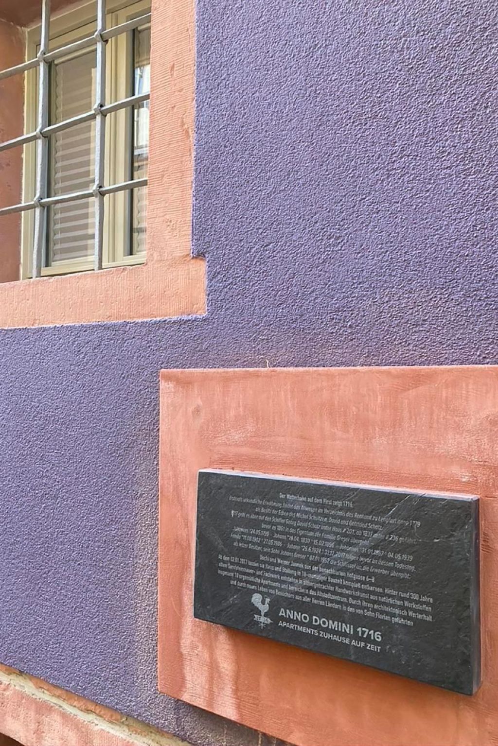 Eine Gedenktafel an einem Gebäude mit violett-orangefarbener Fassade, die angibt, dass es sich um die Apartments Anno Domini 1716 handelt.