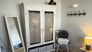 Un dormitorio con un armario blanco, una silla, una lámpara y una cama.