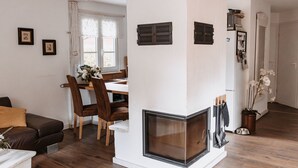 Una sala de estar con chimenea, piso de madera, zona de comedor con sillas y un sofá.