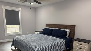 A bedroom with a bed, nightstands, a dresser, a ceiling fan, and a window with blinds.